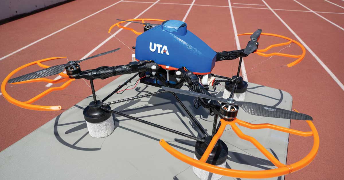 A drone painted in UTA colors with the UTA logo on the side and four propellers lies on the lanes of the UTA track at Maverick Stadium.