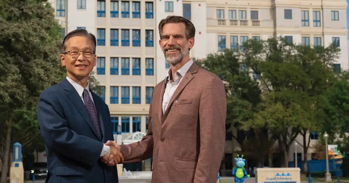 Michael Cho, UTA bioengineering chair, and Dr. Will Stigall, Cook Children's vice president and chief research officer shaking hands in front of a Cook's Children's building.